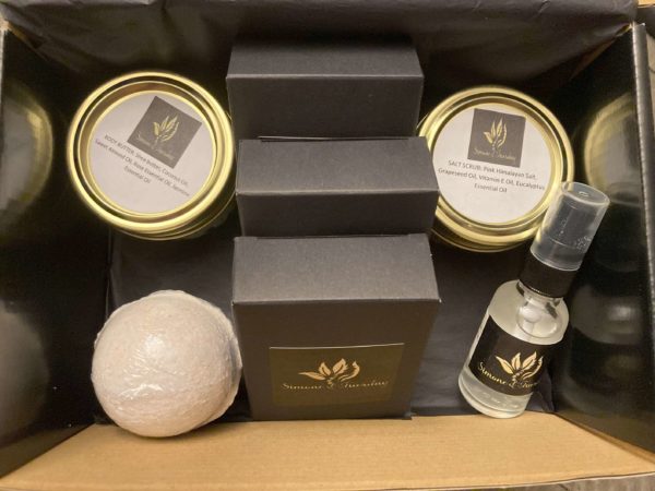 An open black box containing natural body butter, salt scrub, a lavender bath bomb and a bottle of sanitizing spray.