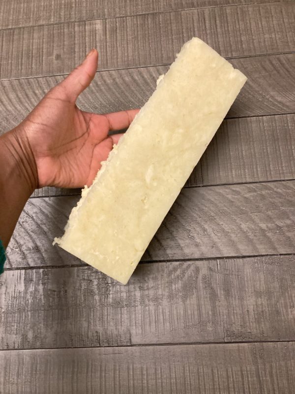 A two-pound loaf of soap being held by a hand to display the size of it. The soap is off-white in the photo.