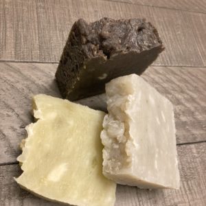 Three bars of natural soaps on a wood table. One brown bar, one gray bar and one-off white bar. All are scented with essential oils.