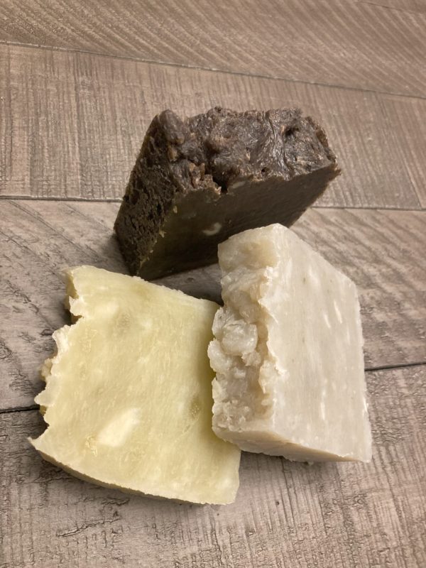 Three bars of natural soaps on a wood table. One brown bar, one gray bar and one-off white bar. All are scented with essential oils.