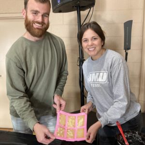 A smiling male and female couple holding newly made soap in a pink colored mold.