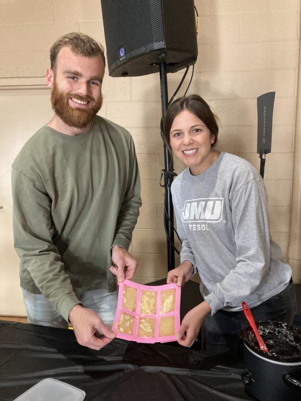 A smiling male and female couple holding newly made soap in a pink colored mold.