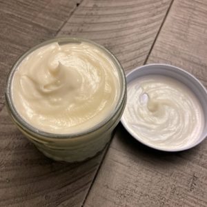 A clear glass jar containing smooth, shiny, yellow colored body butter.