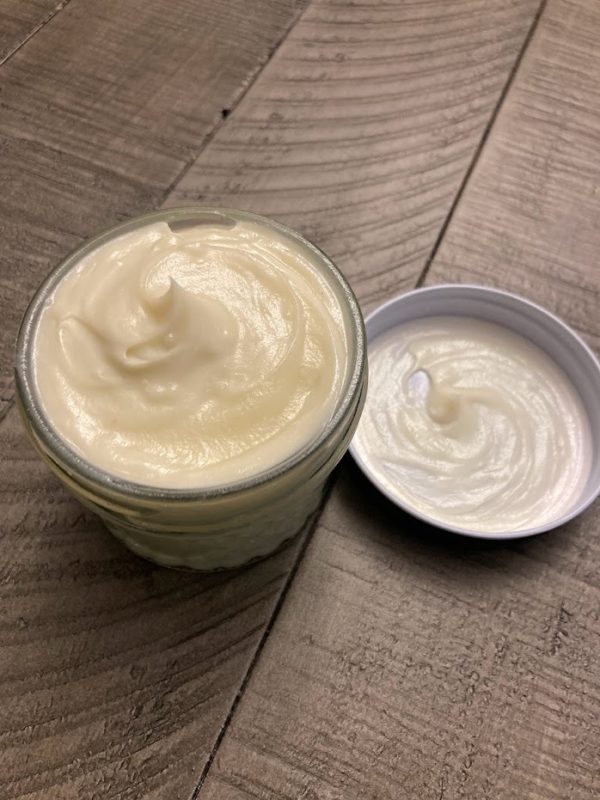 A clear glass jar containing smooth, shiny, yellow colored body butter.