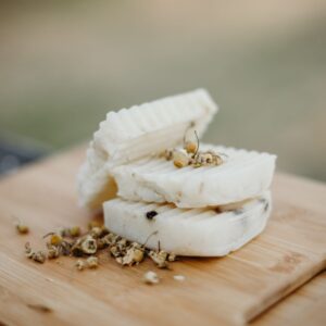 Three bars of Chamomile scented soap with chamomile buds sprinkled over them. The soaps are laying on a wood cutting board.