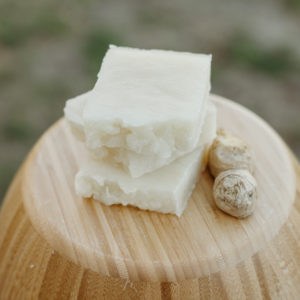 Three bars of natural off-white-colored soap sitting on an inverted wood bowl with a piece of ginger root beside them.