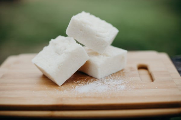 Three bars of natural soap with sea salt sprinkled near them on a wood cutting board.