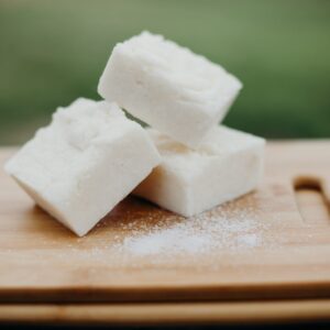 Three bars of natural soap with sea salt sprinkled near them on a wood cutting board.