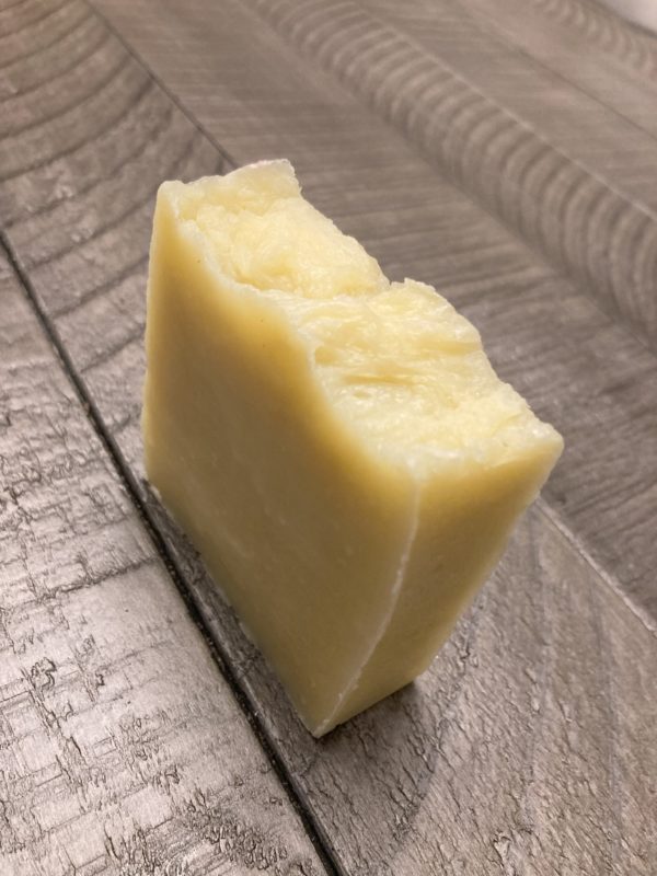 An off-white-colored bar of natural soap sitting on a wooden table.