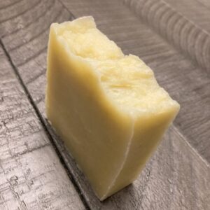 An off-white-colored bar of natural soap sitting on a wooden table.